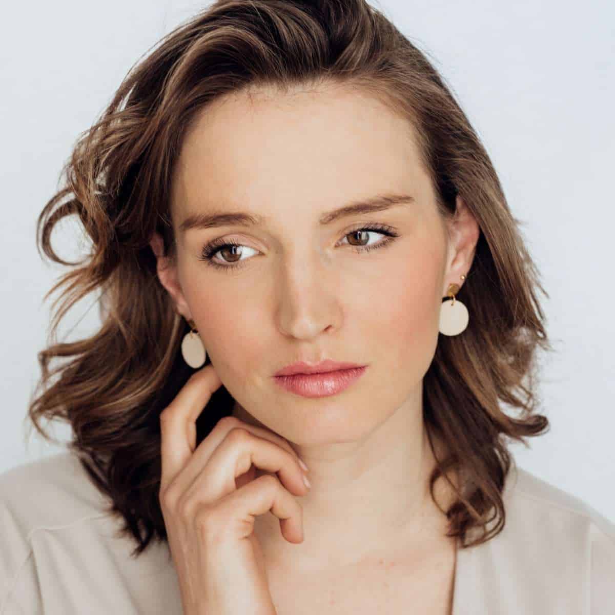 Pure Moon | Christliche Ohrringe – Polymer Edelstahl – beige 5 Elegante Frau mit braunen Haaren und weißen Ohrringen, christliche Lifestyle-Model.
