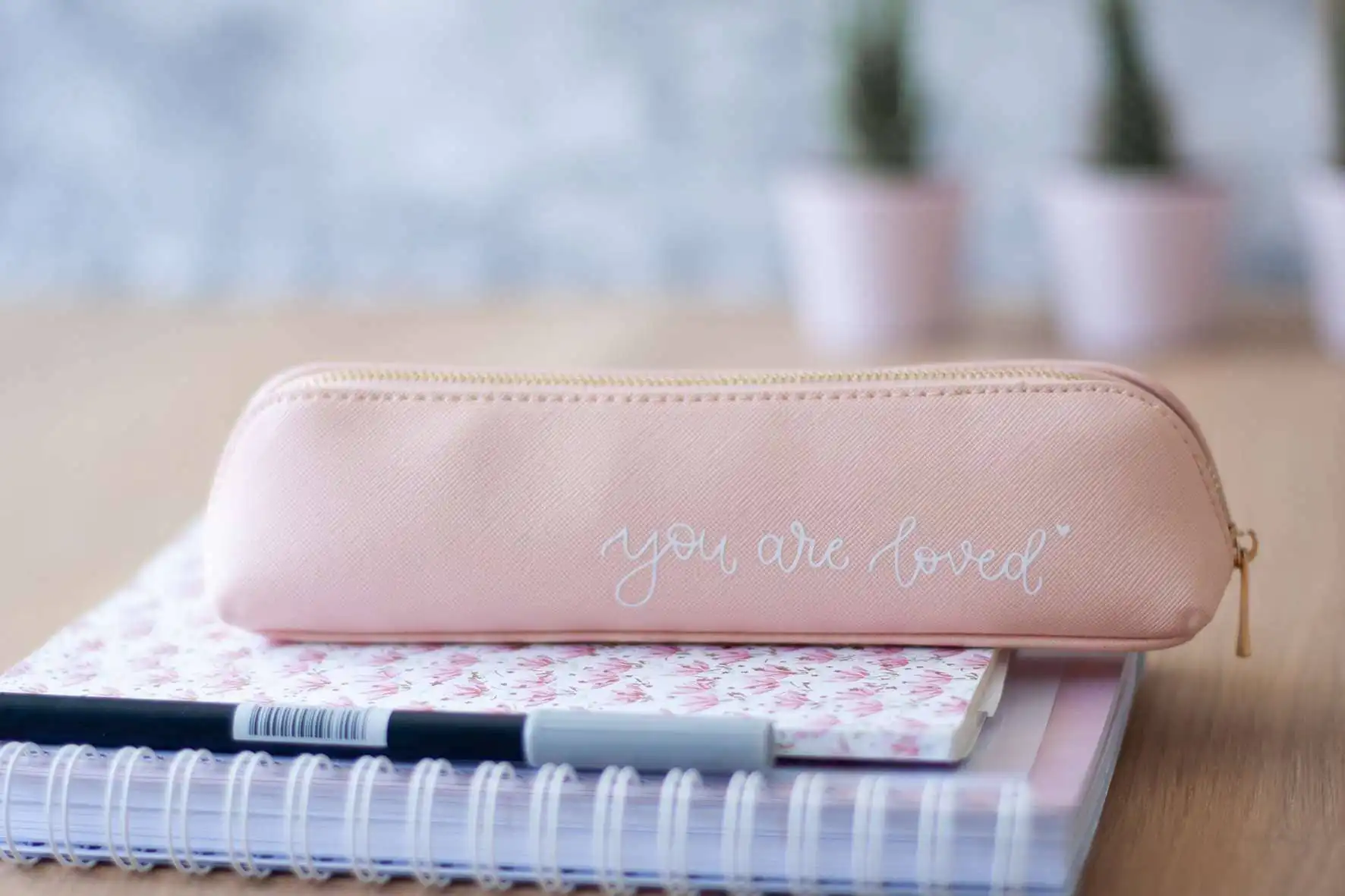 Gottes Blick - Pinkes Kulturtasche mit Schriftzug "You are loved" auf Schreibtisch.