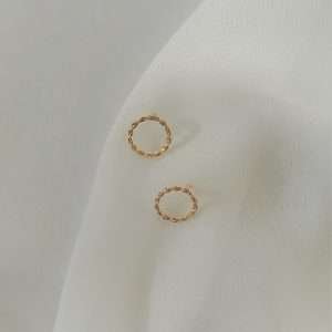 Die eleganten christliche Ohrstecker GOLDEN CIRCLE von FIRSTGOD liegen zusammen auf einem weißen Tuch.