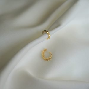 Die christlichen Ohrringe Hoop GLORY von FIRSTGOD und mookho, liegen elegant auf einem weißen Tuch.