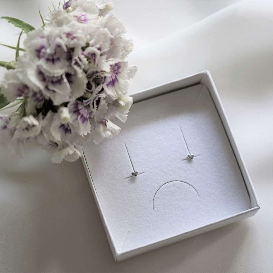 Das Bild zeigt die eleganten und minimalistischen christlichen Ohrstecker LOVE MINI von FIRSTGOD, erhältlich bei mookho. Die Ohrstecker sind nachhaltig verpackt und liegen auf einem Tisch.