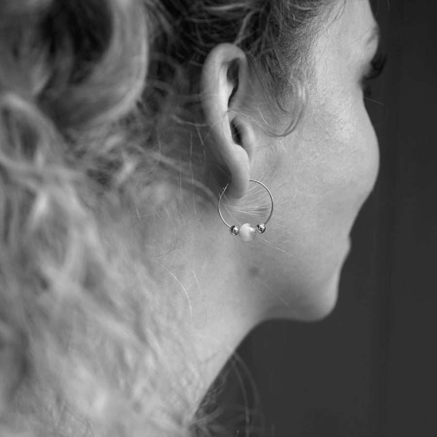 Goldbeschichtete christliche Ohrringe Creolen SARA von FIRSTGOD bei mookho – mit edlen Glasperlen. Die Creolen werden von einer jungen Frau am Ohr getragen, als schwarz-weiß Bild.