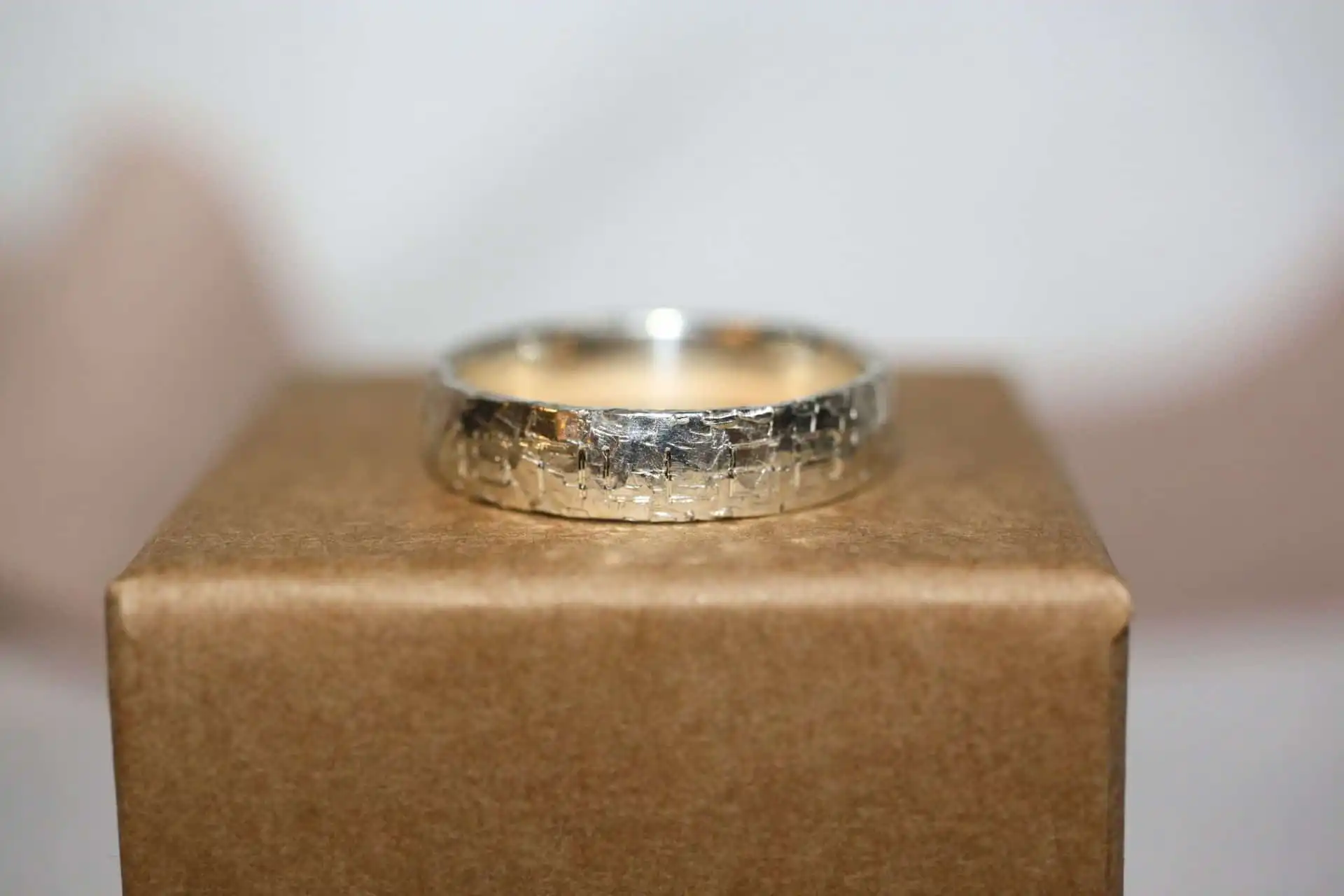 Ring STURMSTILLER 2 Ein silberner Schmuckring auf einem braunen Displaykasten.