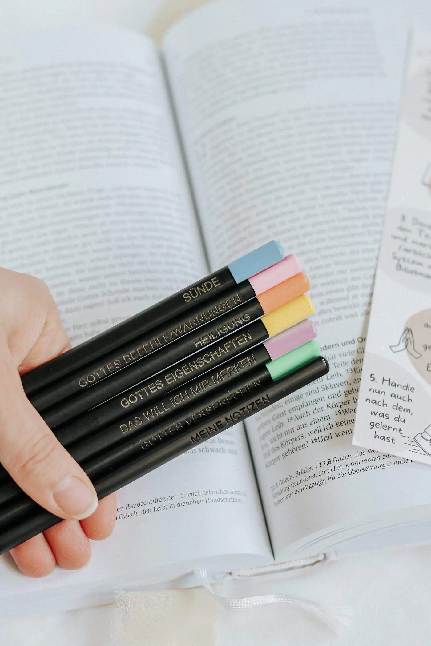 Bibel-Markierstifte mit System • neon 3 Glaubenssymbole und christliche Notizen auf Stiften vor einem offenen Buch.