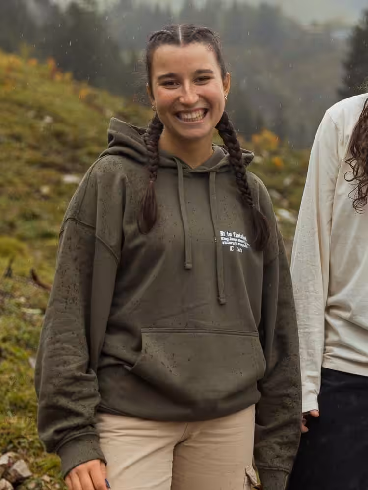 Ansprechende junge Frau mit christlichem Hoodie in Naturkulisse, Glaube, Hoffnung, Liebe.