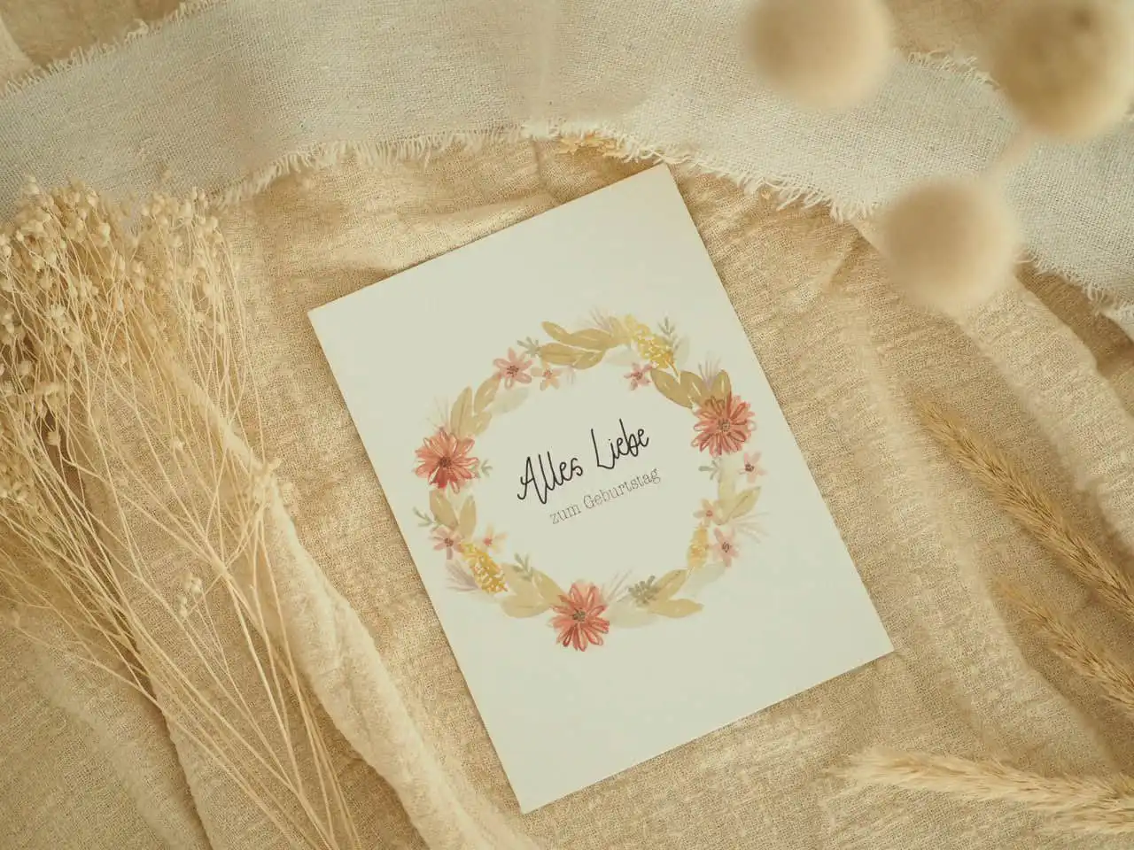 Blumengeschmückte Geburtstagskarte mit dem Text "Alles Liebe zum Geburtstag" auf natürlichem Stoffhintergrund.