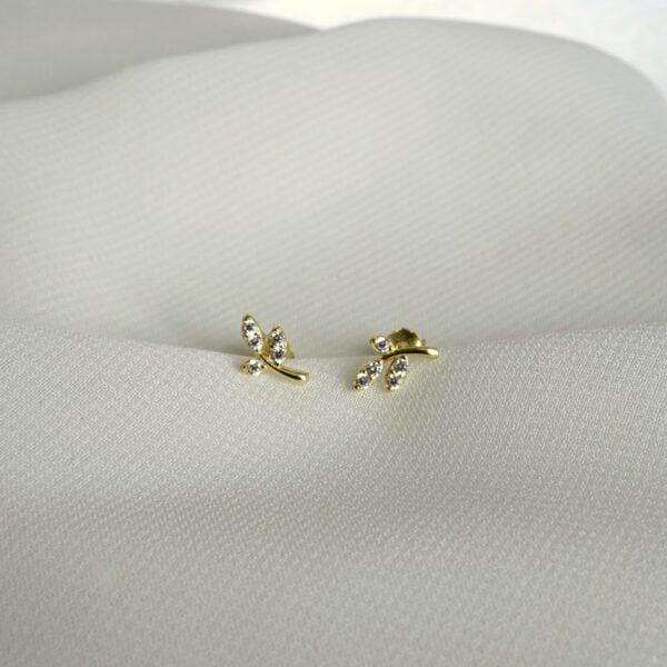 Schimmernde Gold-Ohrringe mit Blattdesign und Zirkonias an weißem Stoff Hintergrund.