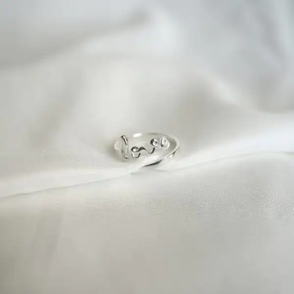 Schlichtes Love-Ring aus Silber auf weißem Stoff, christliche Schmuckmode, Geschenk für Gläubige.