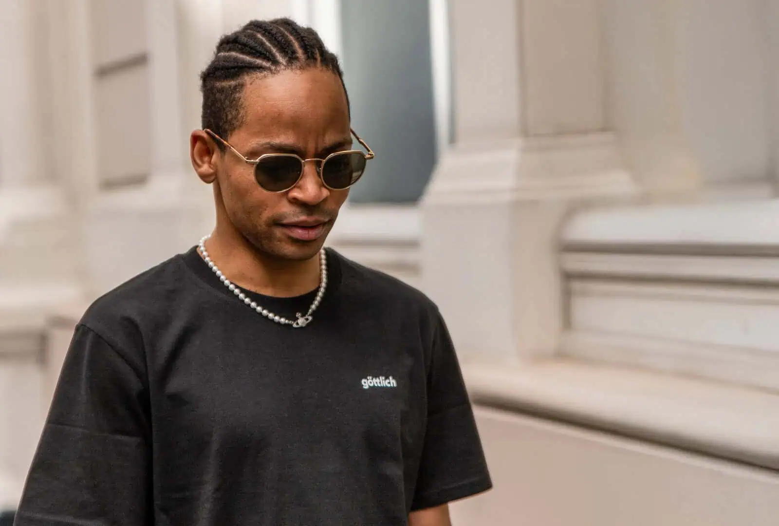 junger Mann läuft mit Sonnenbrille, Kette und seiner schwarzen 'göttlich' Shirt-Kollektion – produziert über mookho.