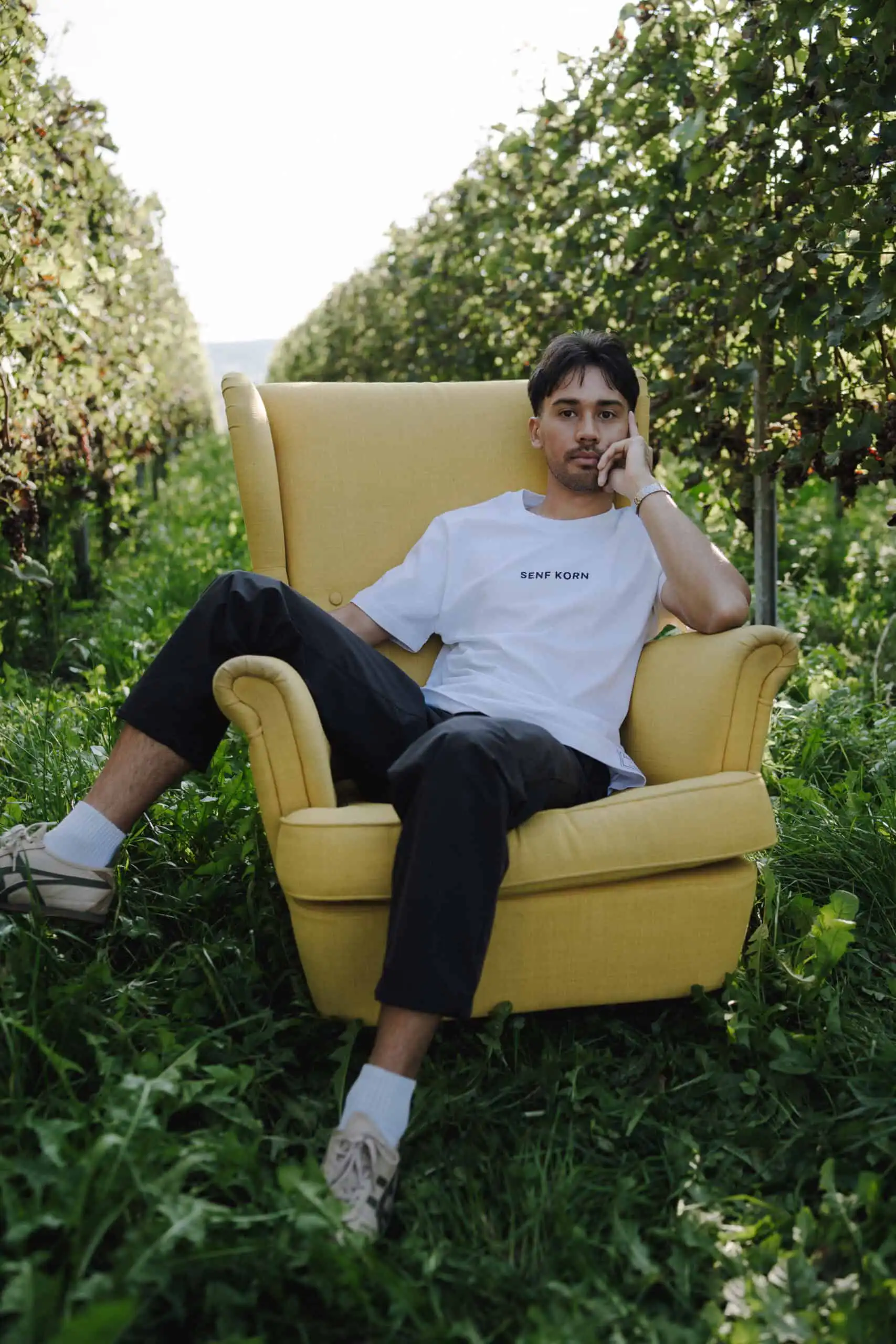 Senfkorn | Christliches T-Shirt – unisex weiß – Bio-Baumwolle – Fair Wear 3 Transparente, modebewusster junger Mann im Outdoor-Garten mit Stuhl, stilvolle Mode.