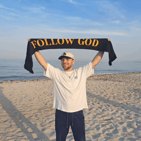 Menschen, der "Follow God" Schal trägt bei Sonnenaufgang am Strand, christliches Leben, Glaubensmotivation.