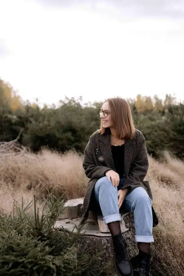 Gemütliche Frau im Wald sitzend, Laub und Natur, hyggelige Stimmung, stilvolle Jacke, casual Style.