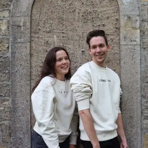 Freundliches Paar trägt bequeme weiße Sweatshirts vor einer Steinmauer.