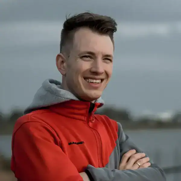 Freundlicher junger mann outdoor, lächelnd, sportliche Jacke, Naturhintergrund, lässige Atmosphäre.