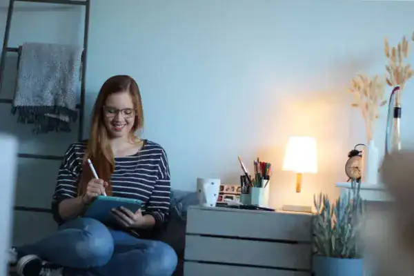 Bequeme junge Frau schreibt am Tablet im Schlafzimmer.