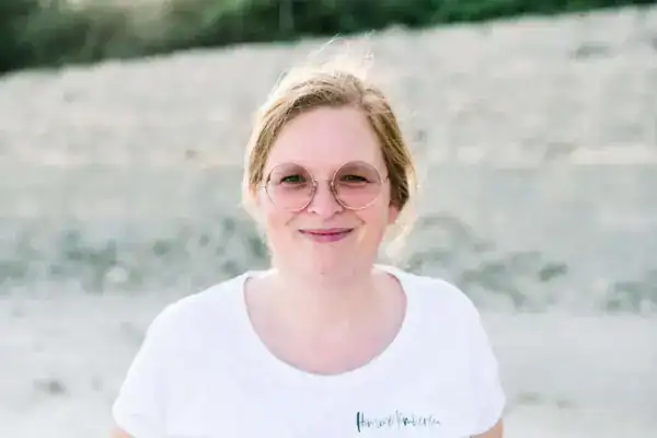 Fröhliche junge Frau mit Brille am Wasser, Sommer, Natur, Lifestyle.