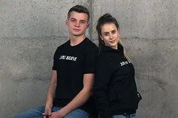 Jungen und Mädchen in schwarzen Hoodies sitzen gegen eine Betonwand.