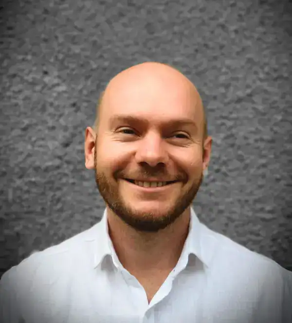 - Professioneller Mann mit freundlichem Lächeln vor grauer Wand.