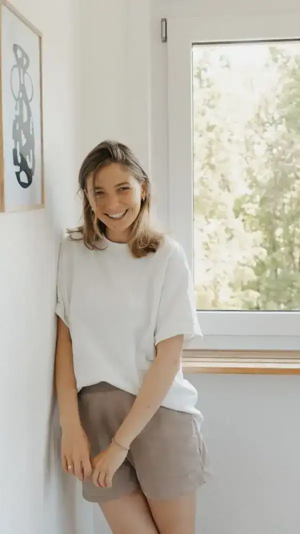 Lächelnde junge Frau in casual Kleidung vor Fenster, modernes Interior, Wohlfühlatmosphäre.