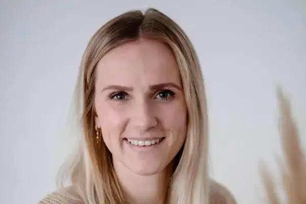 Fröhliche junge Frau mit blonden Haaren lächelt in weißem Raum.