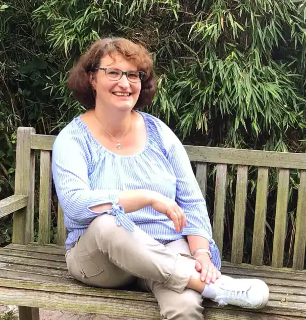 Entspannte Frau sitzt auf einer Holzbank im Garten, fröhlich und entspannt.