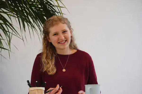 Begeisterte junge Frau mit roten Haaren bei kreativem Arbeiten an einem Tisch, Handschrift und Zeichnung.