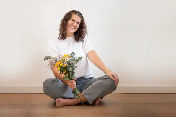Fröhliche Frau sitzt auf Boden mit Blumenstrauß, entspannt, lächelnd, Natur, Glück, Selbstfürsorge.