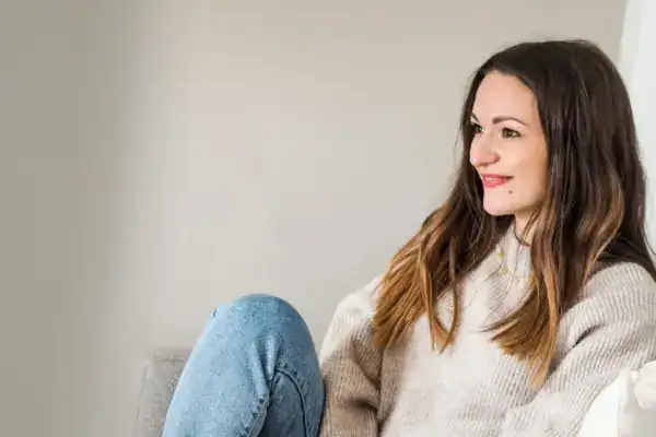 Entspannte junge Frau sitzt bequem auf einem Sofa und lächelt.