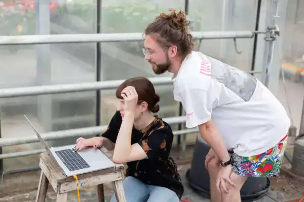 Abendliche Arbeit im Gewächshaus, junge Frau und Mann bei Pflanzenpflege und Recherche.