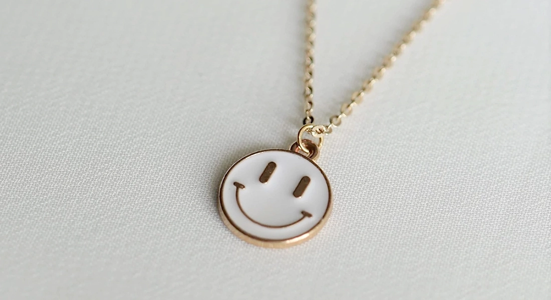 goldene Kette mit Smiley als Anhänger, liegt auf weißem Tuch