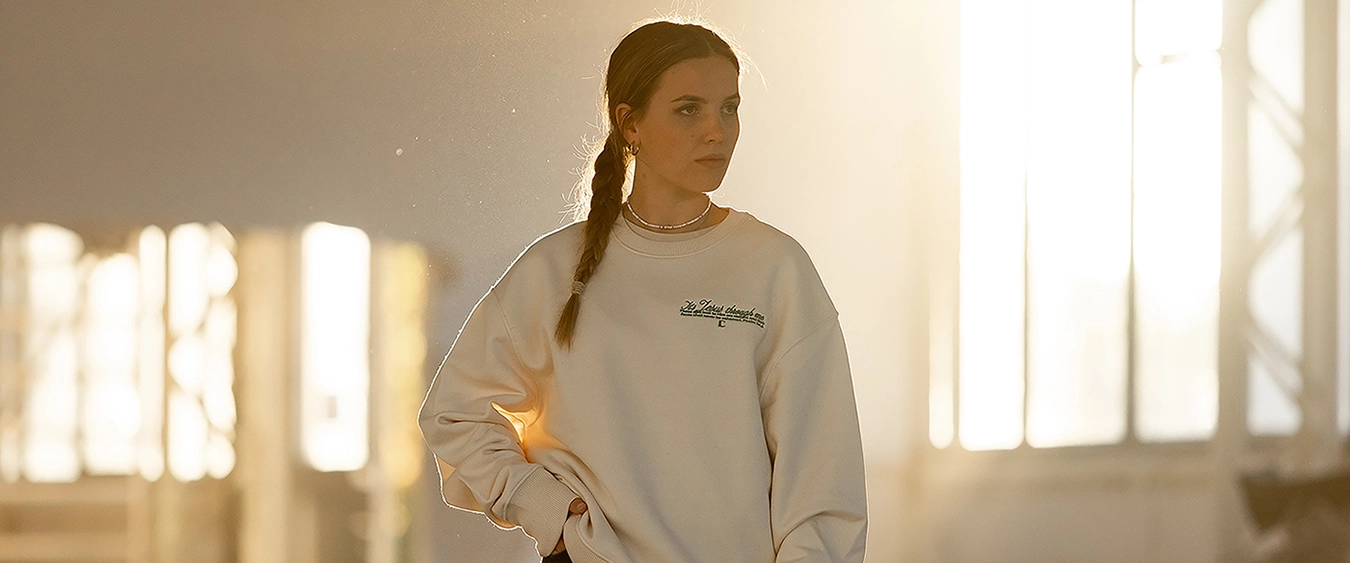 Model trägt beigen It’s Jesus-Pullover in sonniger Industriehalle