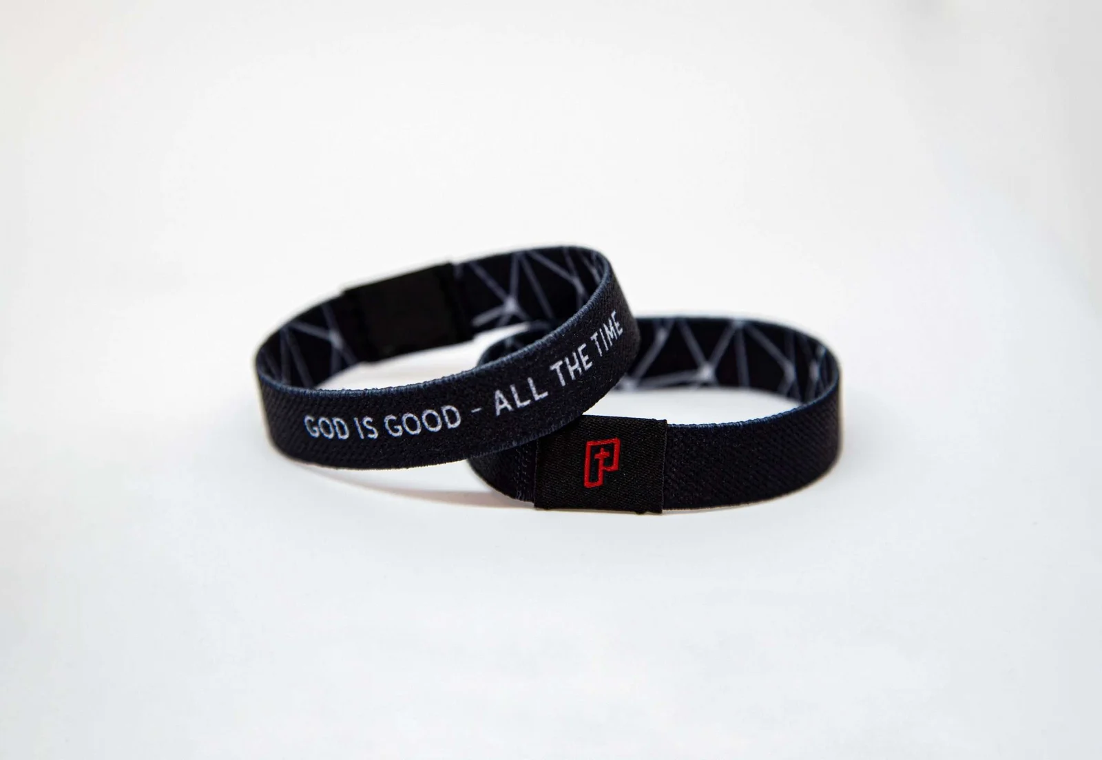 Zwei schwarze Armbänder mit weißer Schrift liegen auf weißem Untergrund