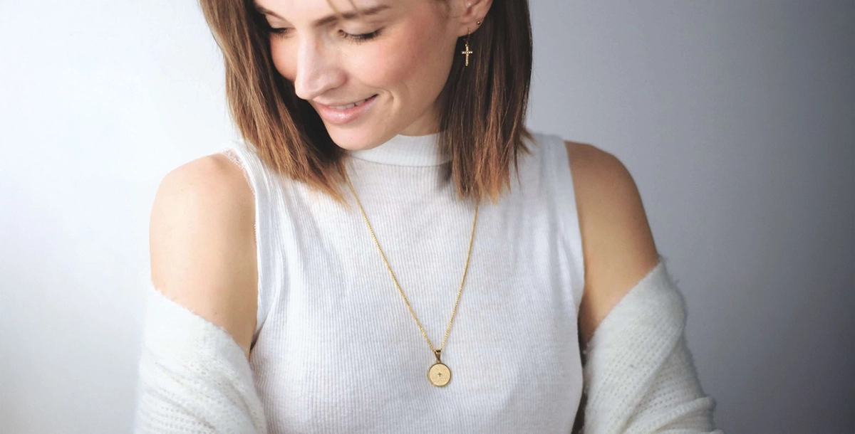 Frau trägt goldene Kette mit Kreuz auf dem Anhänger über weißem Shirt