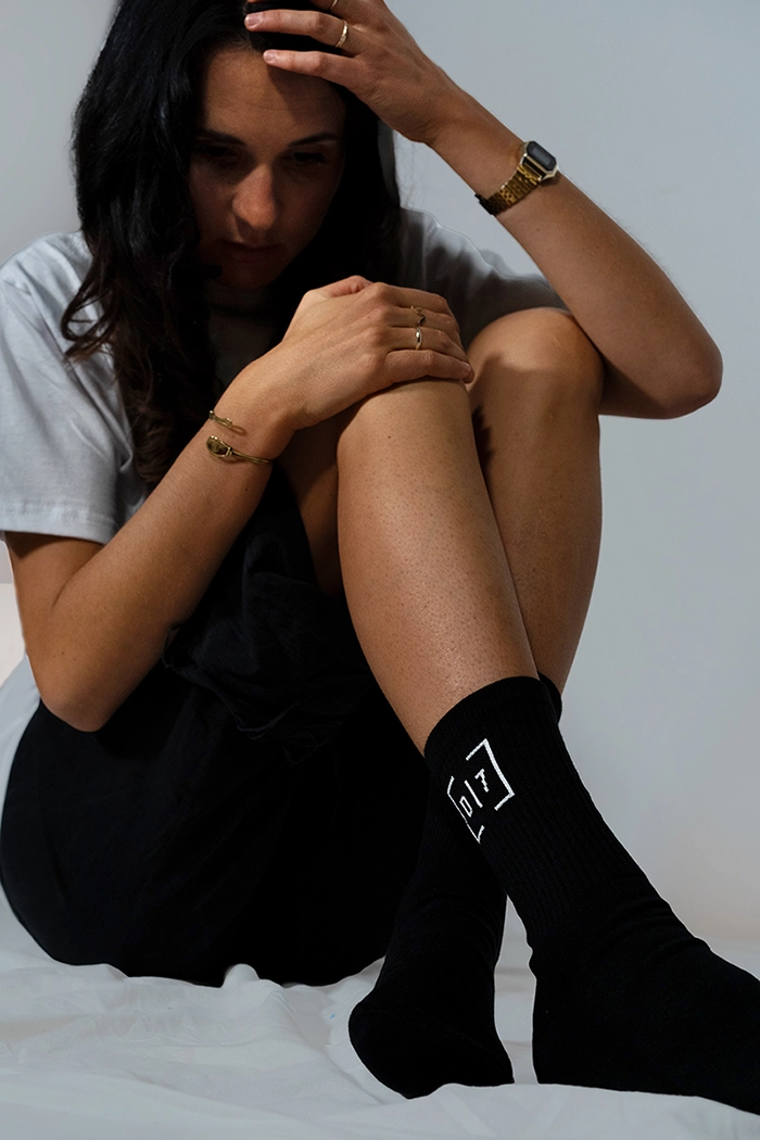 Model sitzt auf dem Boden und zeigt schwarze christliche Socken