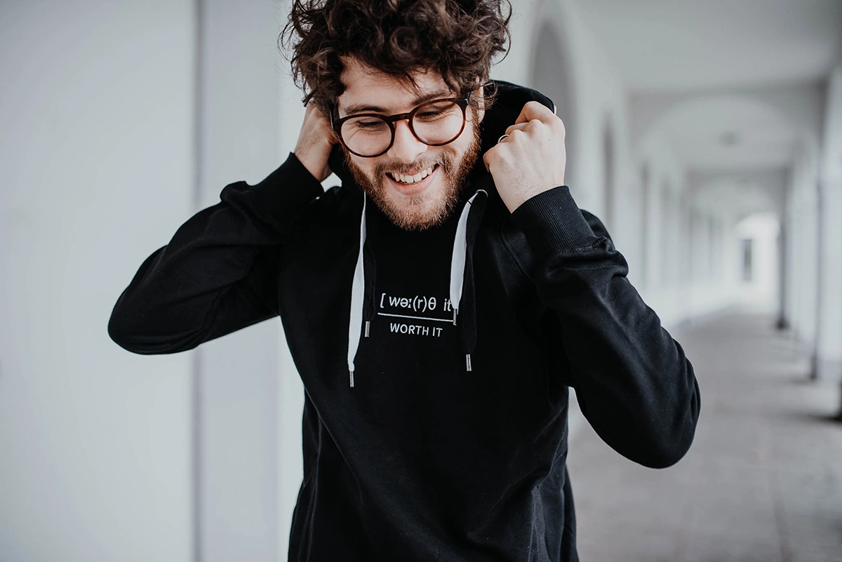 Fröhlicher Mann trägt schwarzen worth it – Hoodie und richtet seine Kapuze