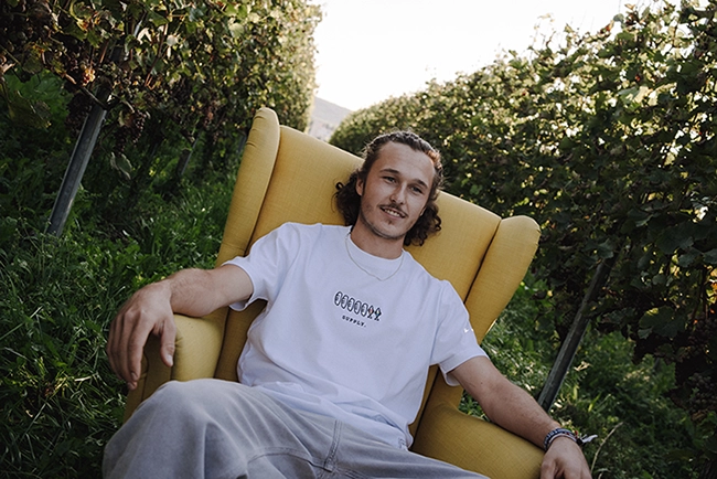 Junger Mann sitzt mit weißem christlichen Shirt im gelben Sessel in den Weinbergen