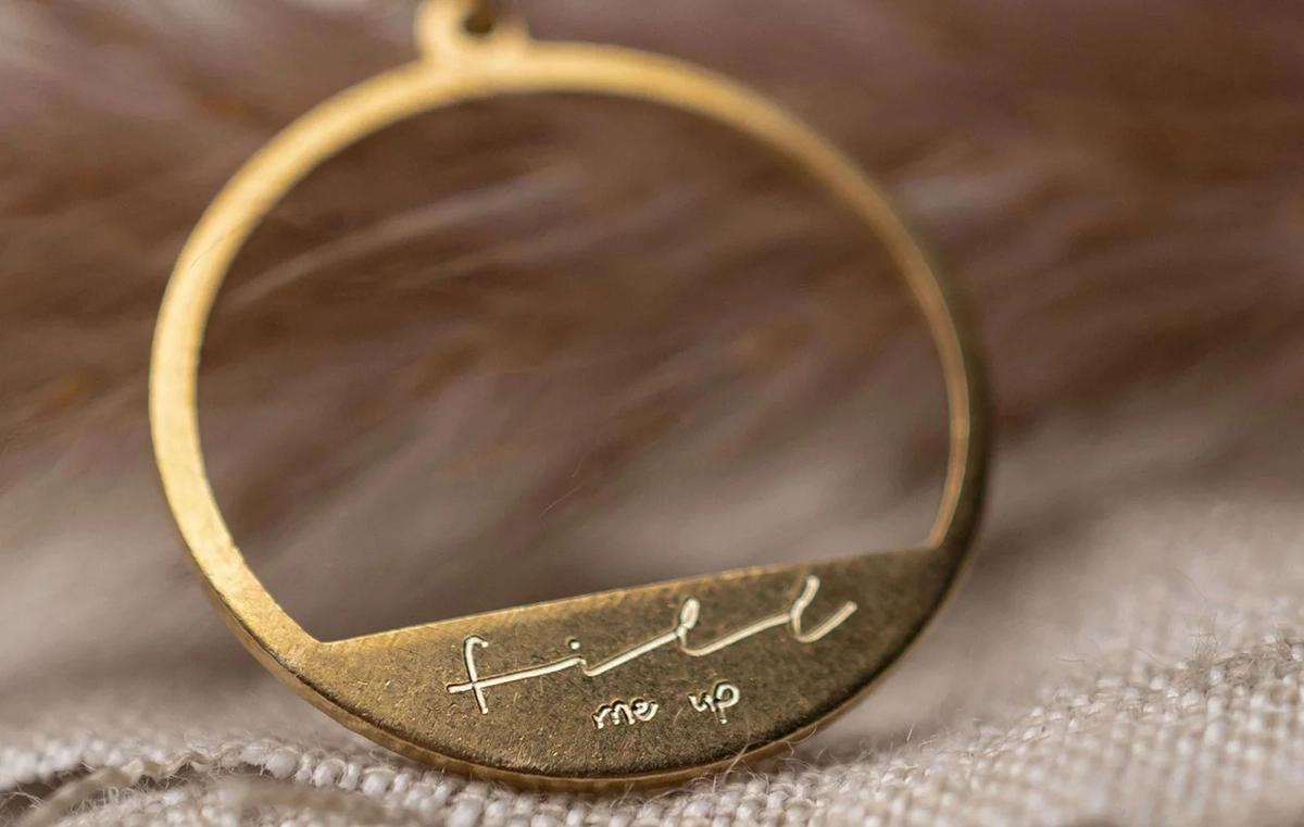 goldener runder Anhänger einer Kette mit Schrift ‚fill me up‘