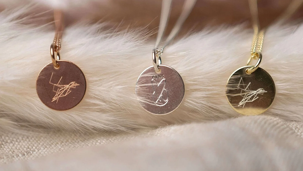 Drei Anhänger einer Halskette in silber, gold und rosé, liegen auf einer weichen Feder