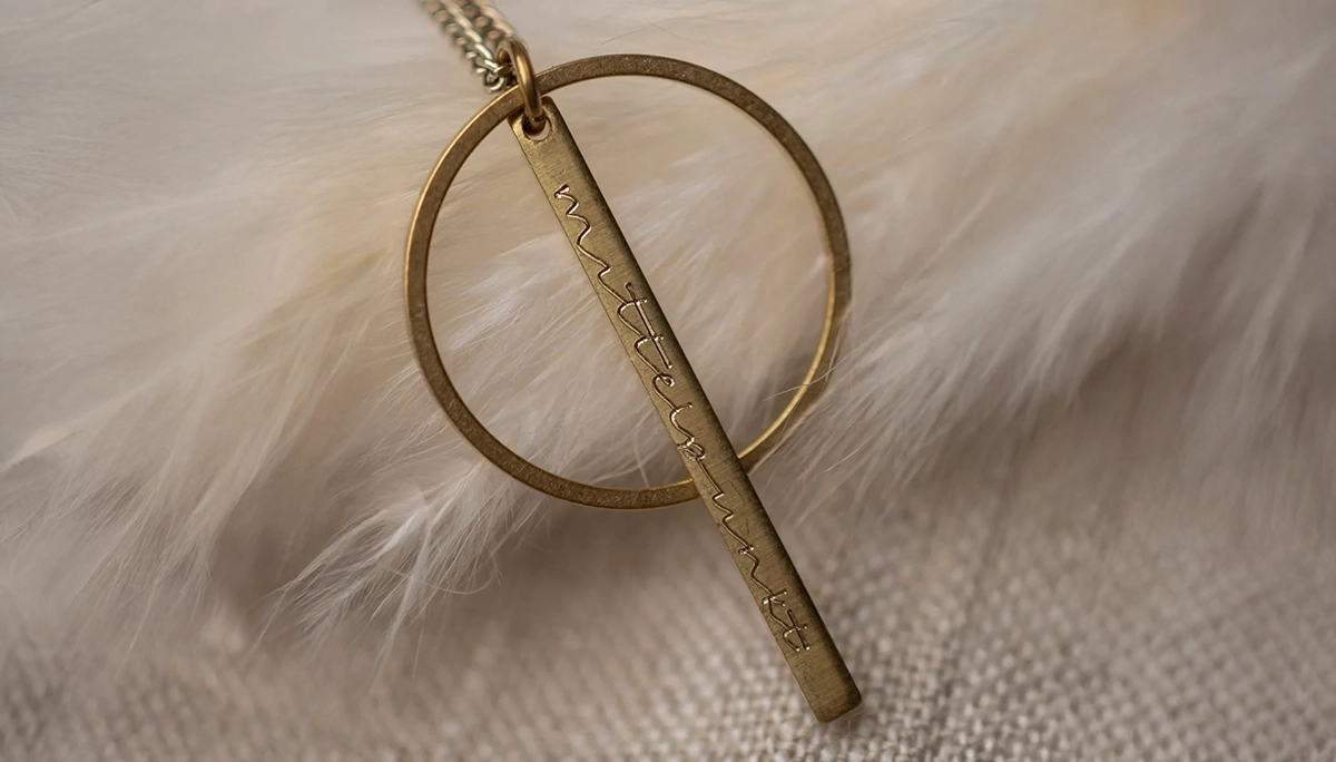 goldener Anhänger mit Aufschrift ‚Mittelpunkt‘, liegt auf weichen Federn