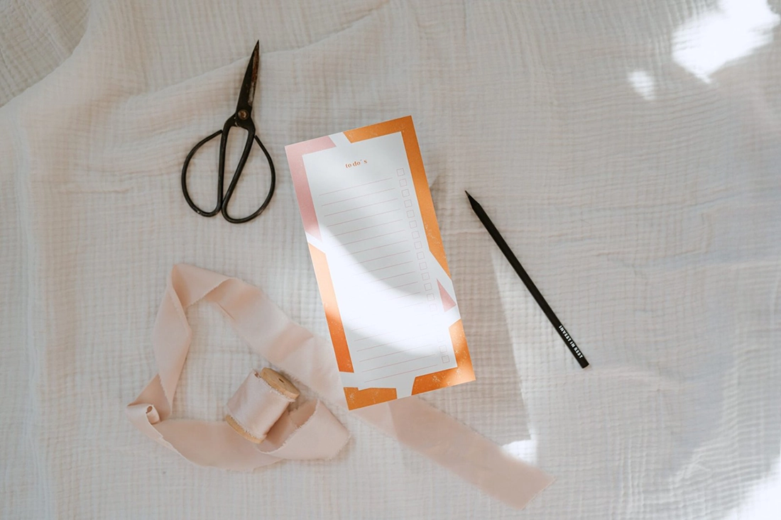 Christlicher To-Do-Block liegt mit schwarzem Stift, Schere und Stoff auf einem weißen Tuch