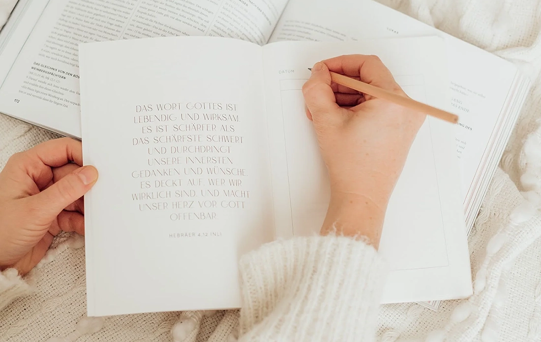 Christliches Notizbuch liegt auf einem Buch und wird mit einem Bleistift beschrieben