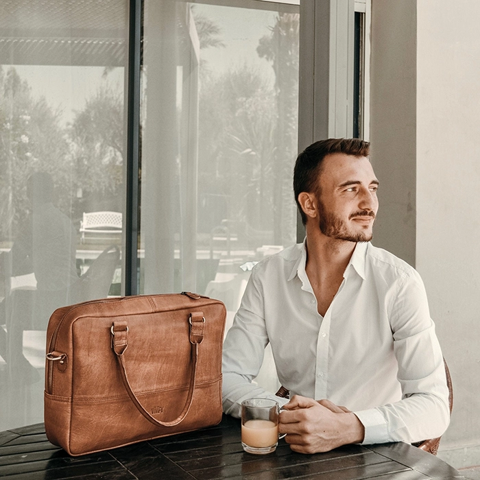 Model sitzt am Tisch neben seiner christlichen Tasche aus Leder