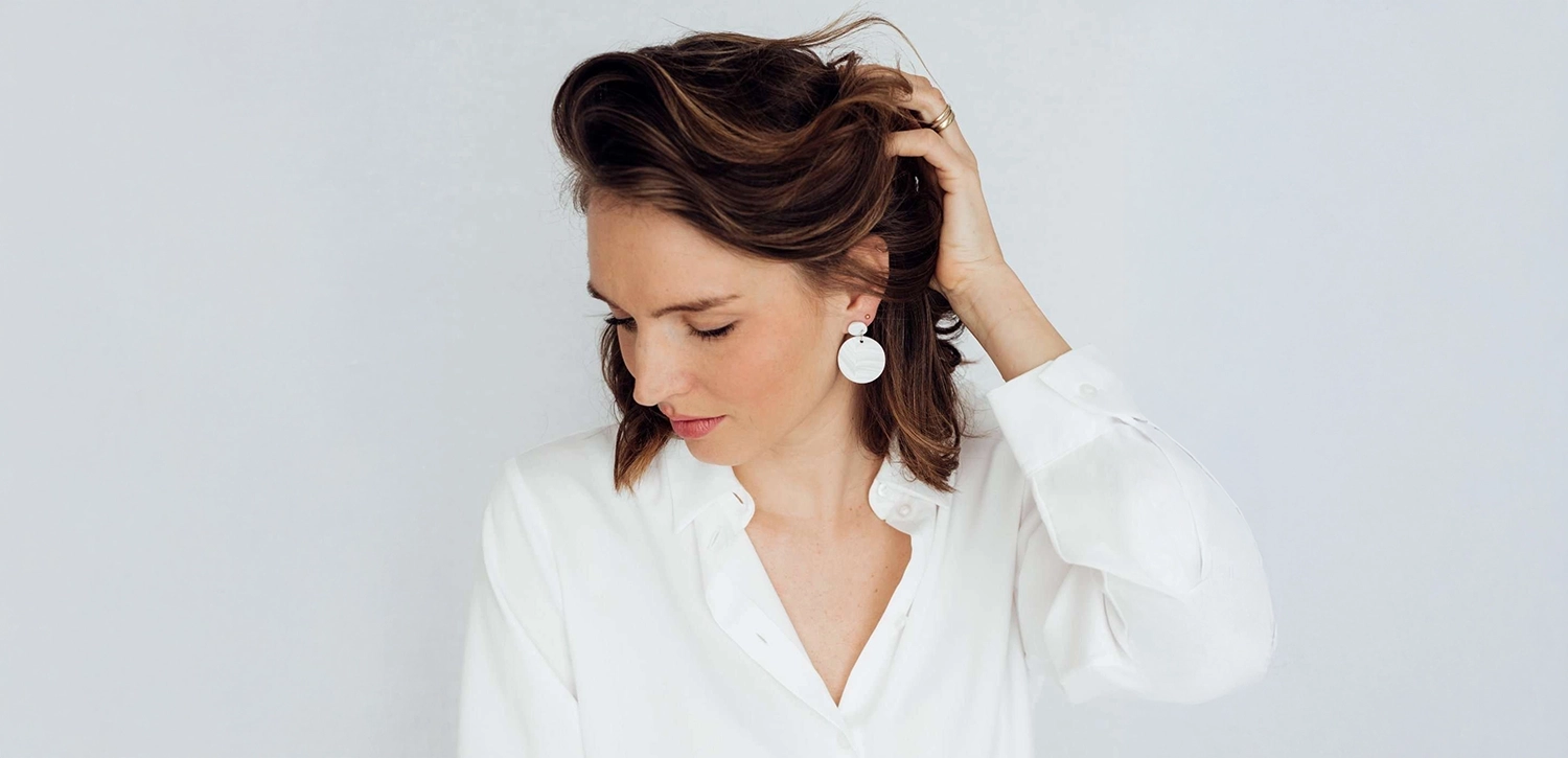 Model trägt weißes Hemd und große runde weiße Ohrringe vor weißem Hintergrund