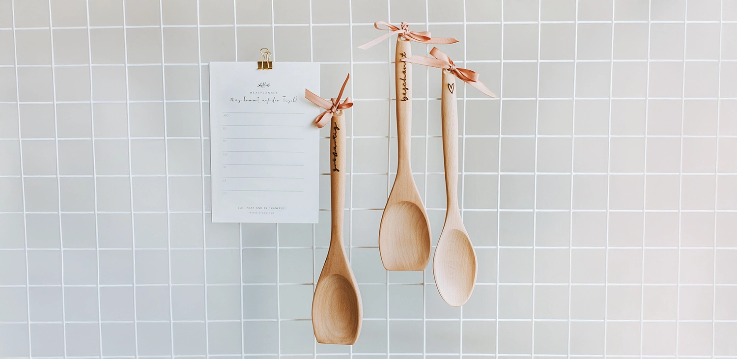 Christliche Küchenhelfer aus Holz hängen an weißem Gitter