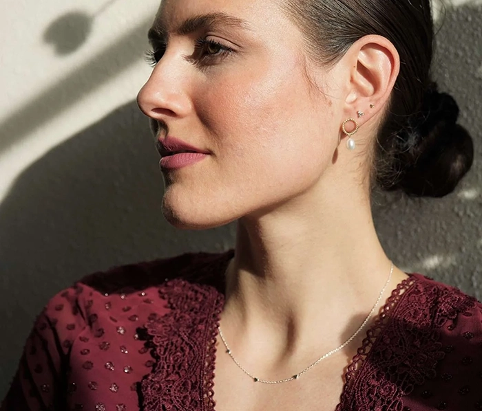 Frau trägt Ohrringe, Ohrstecker und eine schlichte Kette um den Hals