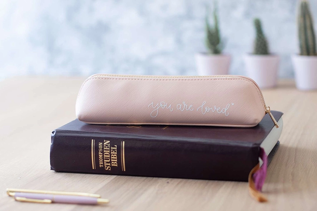 Christliches Mäppchen in rosa liegt auf einer schwarzen Studienbibel