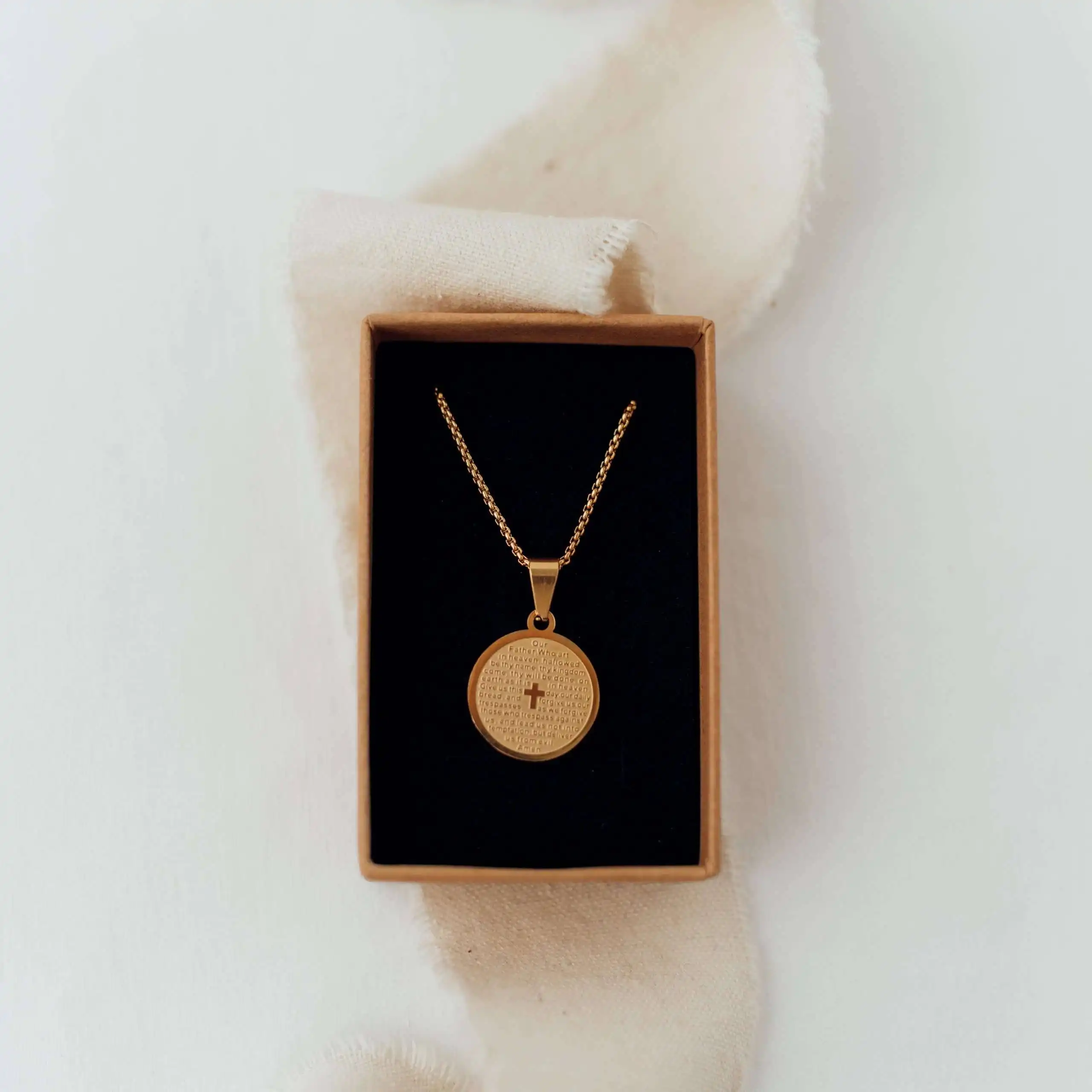 Halskette mit Kreuzanhänger in Gold in Schmuckschachtel auf weißem Stoff.