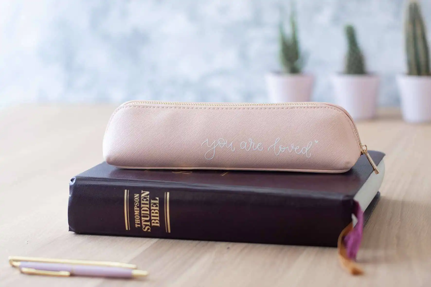 Ein eleganter pinker Etui mit der Aufschrift "you are loved" auf einem Bücherstapel, christliche Ins.