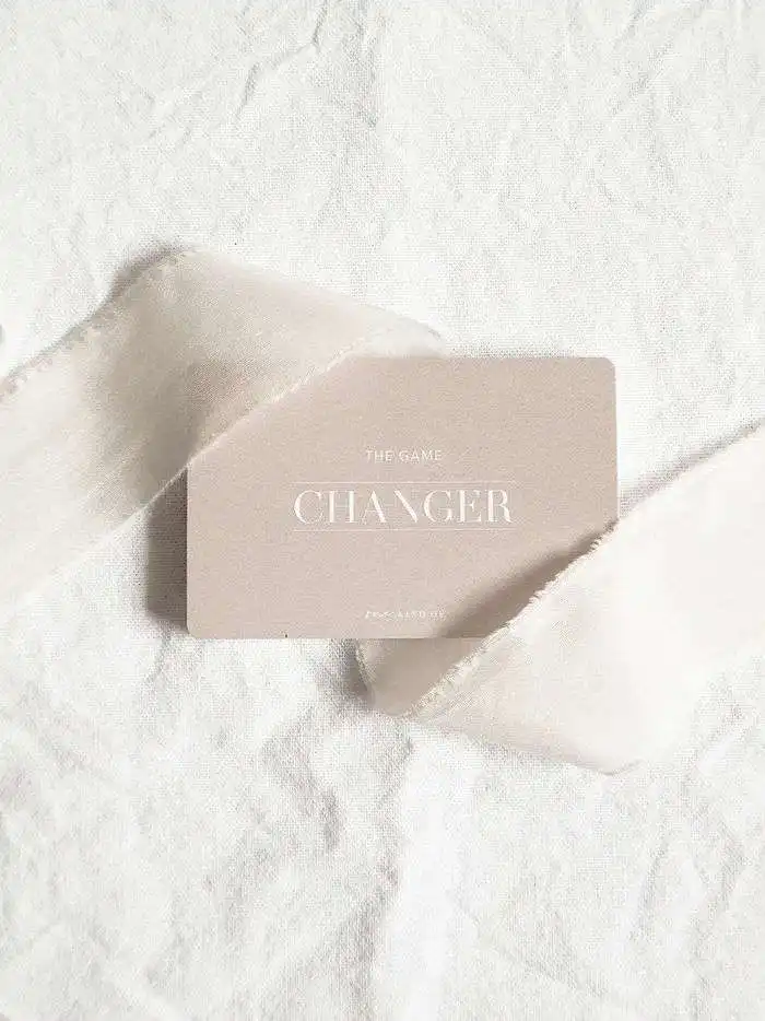 Ein minimalistisches Kartenspiel "Changer" auf weißem Sand mit zerfetzten Papierstücken.