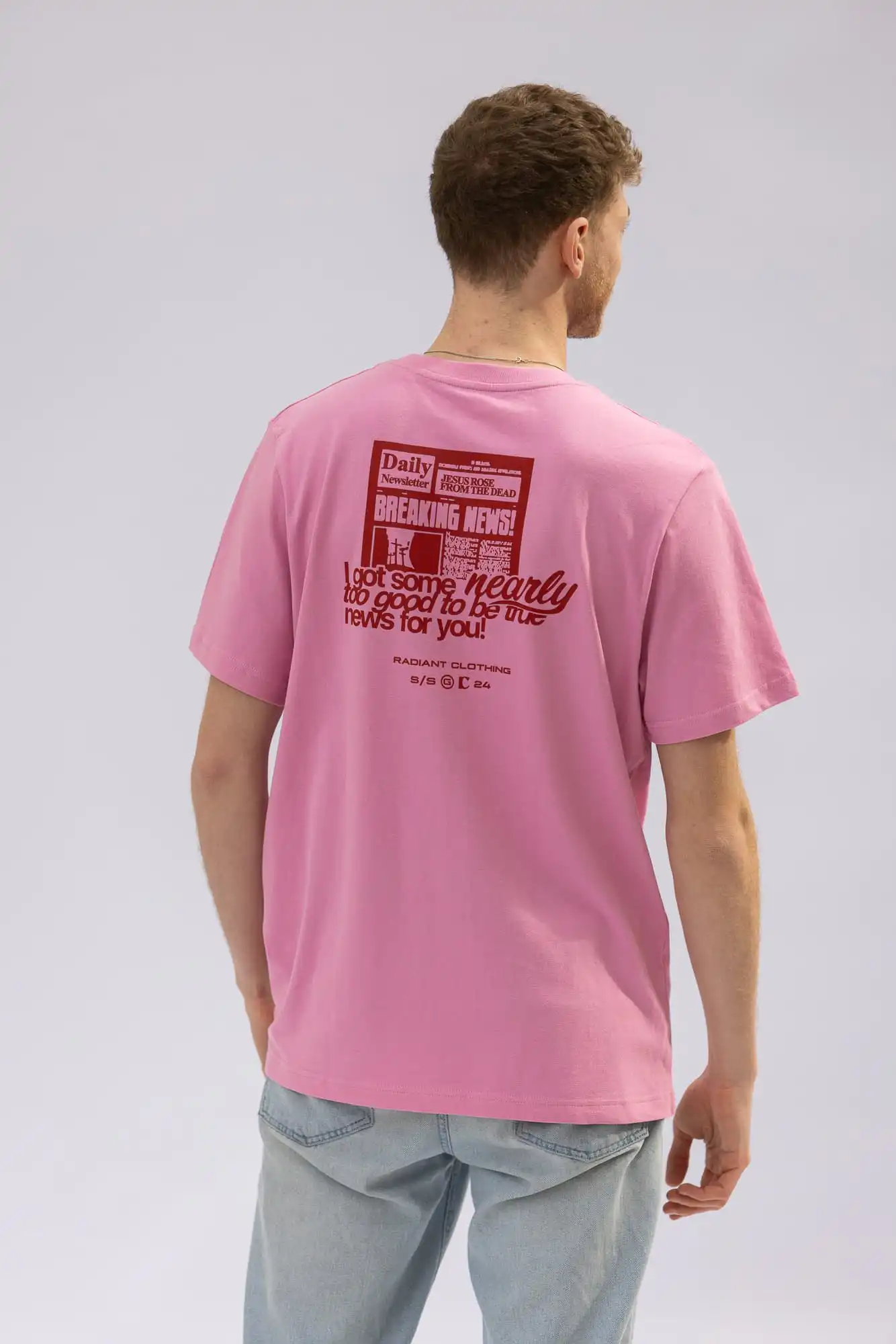 Ein junger Mann trägt ein pinkes T-Shirt mit christlichem Design, Blick nach rechts gerichtet.